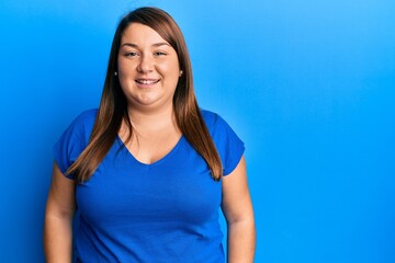 Beautiful brunette plus size woman wearing casual blue t shirt with a happy and cool smile on face....