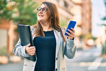 Young plus size businesswoman using smartphone holding binder at the city