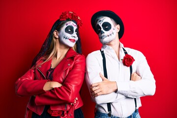 Couple wearing day of the dead costume over red looking to the side with arms crossed convinced and confident