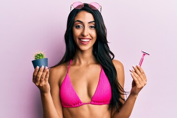 Beautiful hispanic woman wearing bikini holding cactus and razor smiling and laughing hard out loud because funny crazy joke.