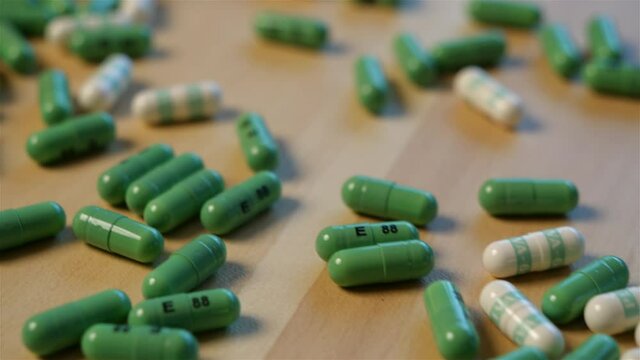 Dolly shot approaching a spilt bottle of white and green prescription pill tablets on a wooden tabletop