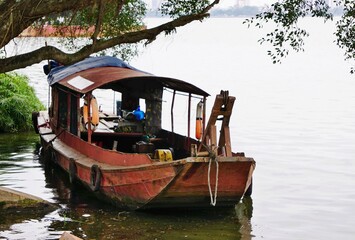 Vintage rusty workboat in silhouette along the shore under a tree in Vietnam