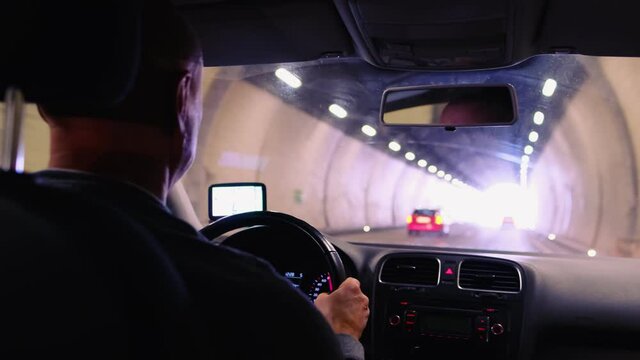 car driver driving through a long, lamp-lit tunnel in the Swiss mountains, selective focus on the vehicle dashboard, auto travel concept, positive exit, road traffic