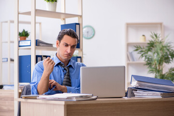 Fototapeta premium Young businessman employee unhappy with excessive work in the o