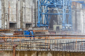 Two builders talk against the backdrop of a water dam under construction.