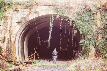 explorer with backpack at the entrance of abandoned dark tunnel