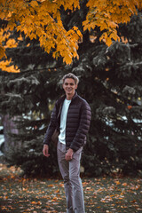 Male with bleached hair smiling in a park during the fall season wearing a brown outfit