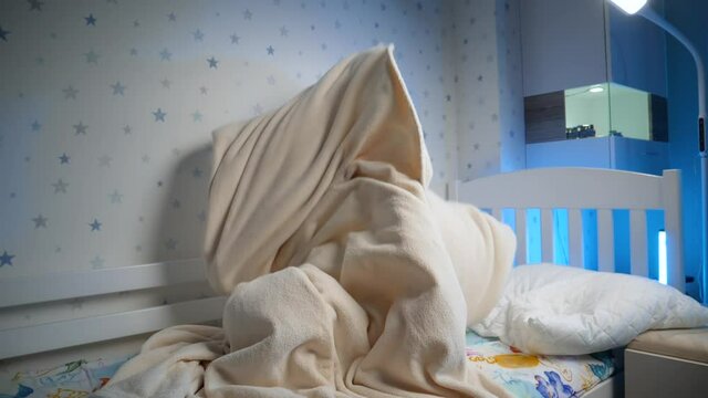 Slow motion of little toddler boy hiding under blanket and jumping out. Child playing and scaring people at night