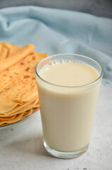 A glass of milk is on a gray countertop next to a plate of pancakes, a blue towel in the back.