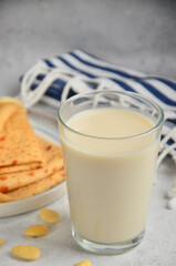 A glass of milk on a stone gray table, next to a plate of crepes.