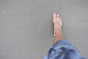 perna e pé de um homem usando bermuda azul e pisando na areia. Espaço para texto. 
