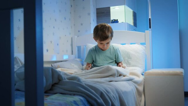 Little 5 years old boy using and playing on tablet computer before going to sleep at night. Child with gadget at evening