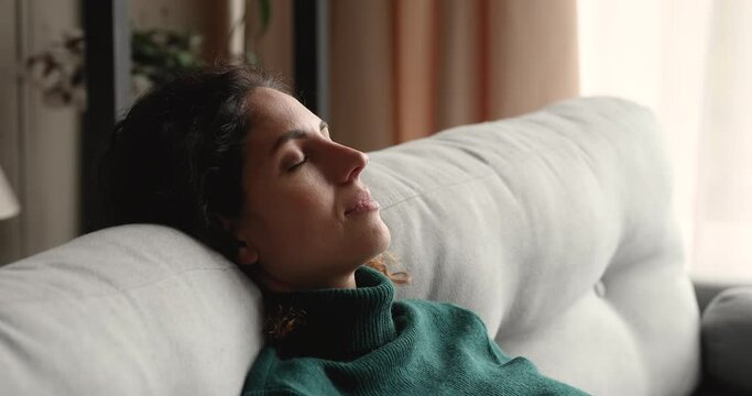 Close up side profile view female with eyes closed fall asleep leaned on couch smiling thinking pleasant thoughts, breathing deeply fresh air, enjoy leisure lazy day at modern home, relaxation concept