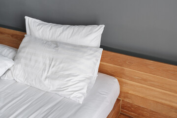 Close-up modern white bed, wooden bedhead and gray wall