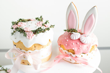 Easter cake, sweet bread decorated with bunny ears cookies, sugar icing and meringues. Kulich wrapped in a craft paper on the white background. Panettone filled with dried fruits and raisins