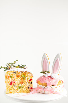 Easter cake, sweet bread decorated with bunny ears cookies, sugar icing and meringues. Kulich wrapped in a craft paper on the white background. Panettone filled with dried fruits and raisins