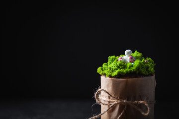 Easter cake, sweet bread decorated with green grass sugar icing and rabbit. Kulich wrapped in a craft paper on the dark background.