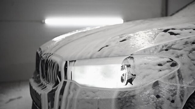 The car headlights is covered with white washing foam close-up