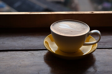Close up yellow coffee cup with heart shape latte art foam on the table.
