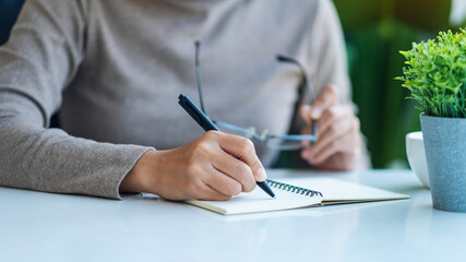 Closeup image of a woman writing on a blank notebook on the table