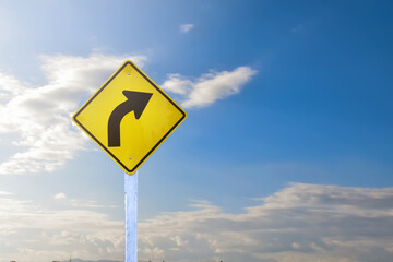 Right turn sign on white pole with clouds and blue sky background.