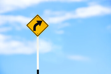 Right turn sign on white pole with clouds and blue sky background.