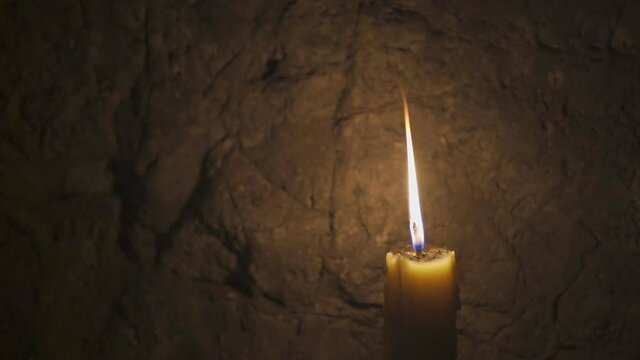 yellow candle in dark cave calm with burning candle flame on night peace and stone wall background for warm white light and holy thing with pray at temple or church on slow motion