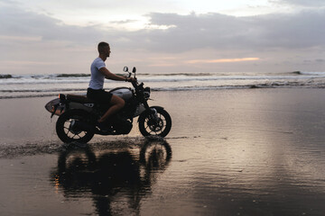 Fototapeta na wymiar Surfer rides on motorbike with surfboard at sunset ocean beach. Bali island, Indonesia