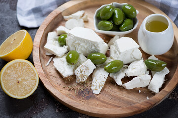Blocks of feta cheese with giant olives, olive oil and lemon on a wooden serving tray, closeup, horizontal shot