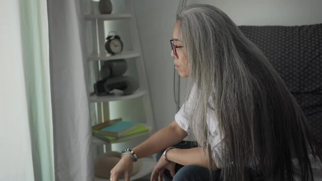 Worried grey-haired woman sits on the bed and smokes a cigarette,Thinking about work and suffering during COVID.