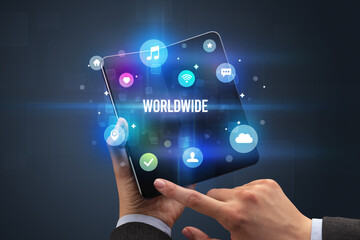 Businessman holding a foldable smartphone with WORLDWIDE inscription, social media concept