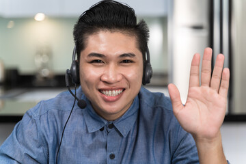 Asian men are greeting during a video conference in the kitchen during work from home. He is trainer wearing a headset is greeting while teaching online in video conference and technology concept..