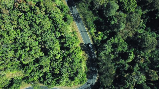 Establishing aerial top view shot of country side road passing through the green forest and mountain.