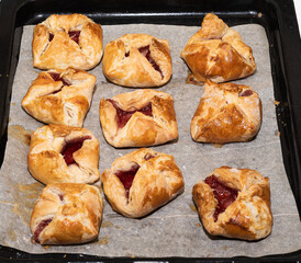 Baked dessert envelopes with jam on a baking sheet.