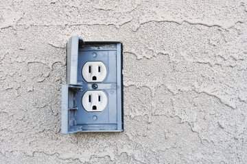 An image of a grey out door electrical socket on a grey stucco wall. 
