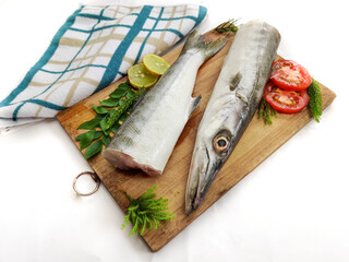 Fresh raw Barracuda Fish (cheelavu) head and body decorated with herbs and vegetables on a White background.Selective Focus.