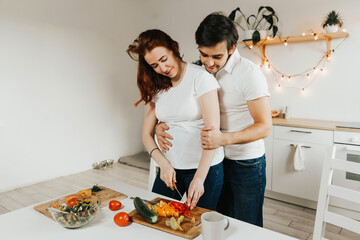 pregnant woman and man preparing salad in the kitchen. husband and wife of European appearance cut vegetables