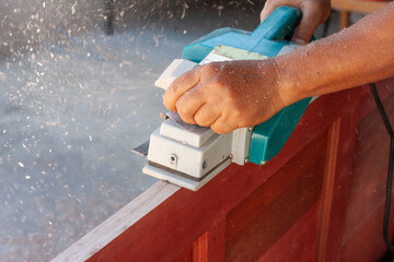 The hands of a carpenter were using an electric planer to smooth out the wood.