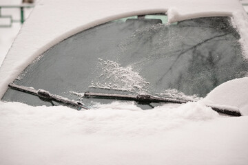 Car wiper blades clean snow from car windows. Flakes of snow covered the car with a thick layer....