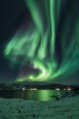 Enorm noorderlicht (aurora borealis) over een strand en een fjord in arctisch Noorwegen