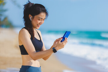 Young Asian sport woman using fitness app on wearable technology on smartphone, Female runner use smart device gadget for running at beach