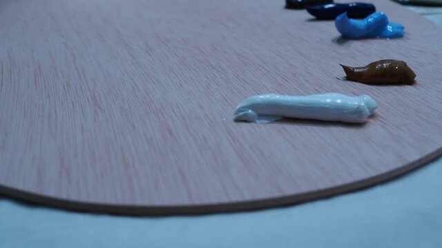 the girl's hand squeezes out oil paints on a palette for drawing. side view of shooting.