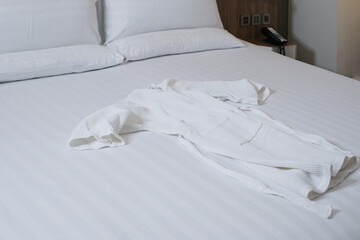 Fototapeta na wymiar Clean towel on bed in modern hotel bedroom. White bed sheets and pillows. White bathrobe on the hotel bed. Comfortable bed with clean bathrobe in hotel.