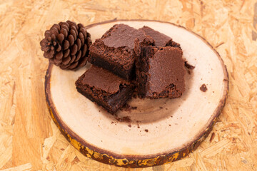 Pieces of fresh chocolate brownie on wooden plate on white background. Stack of fudgy chocolate brownies on white background, homemade bakery and dessert. Brownie chewy squares stack on wooden plate.