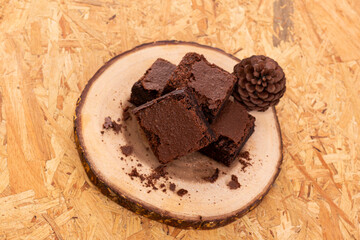 Pieces of fresh chocolate brownie on wooden plate on white background. Stack of fudgy chocolate brownies on white background, homemade bakery and dessert. Brownie chewy squares stack on wooden plate.