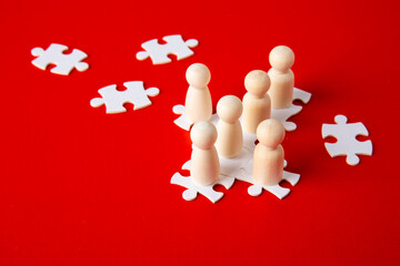 Wooden figures on puzzles on red background as a symbol of team building. Organization group people in business.
