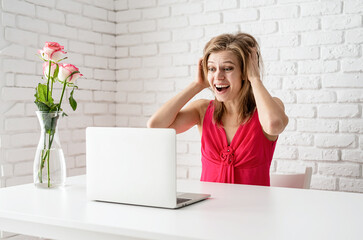 Surprised beautiful blond woman in pink dress dating online using laptop