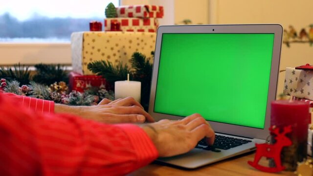 Man hands typing on laptop keyboard with blank green screen on Christmas background. Chroma key monitor. Free content. Mockup monitor. Online greeting. Internet surfing. New Year Celebrating concept.