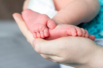 Tiny feet of a newborn baby in the hands of a mother.