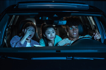 Portrait of three young friends looking emotional while sitting together in the car and watching a...